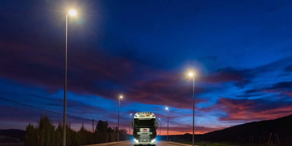 Truck with dangerous goods circulating at night under the light of street lamps on a street in an industrial estate.
