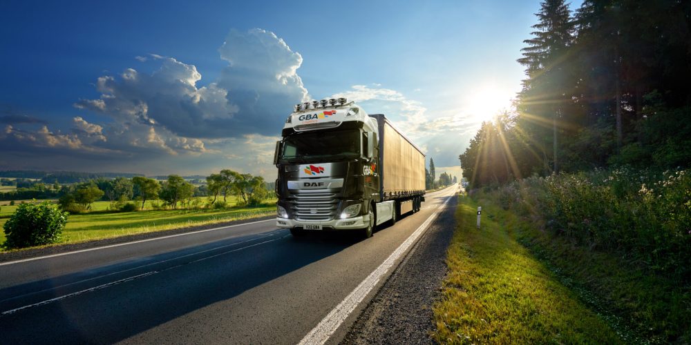 White truck arriving on the asphalt road in rural landscape in the rays of the sunset