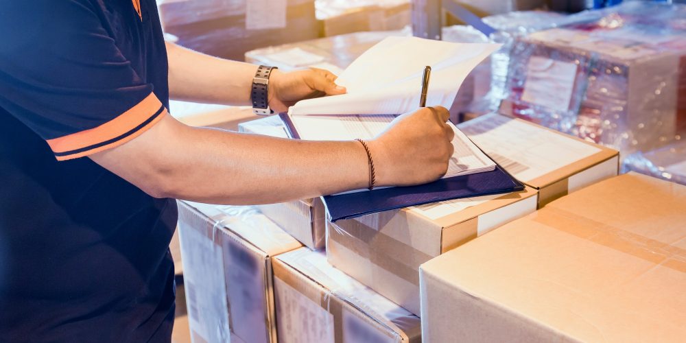 Warehouse worker writing on clipboard his checking details shipm