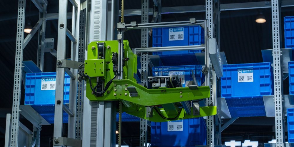 High-tech automated warehouse system featuring a green robotic arm handling blue storage crates.